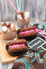 Chocolate sandwich cookies with pink butter cream in black iron mini skillets. Bottle of milk and glass of milkshake with marshmallows on the background.