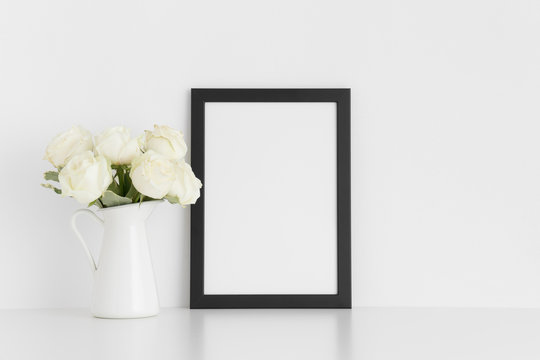 Black frame mockup with a bouquet of white roses in a vase on a white table.Portrait orientation.