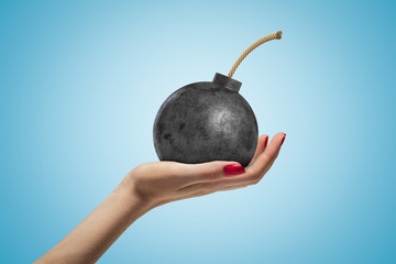 Female hand holding ball bomb with fuse on blue background