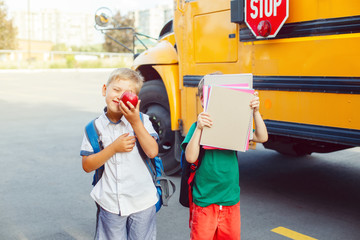 Two funny happy Caucasian boys students kids with apples standing near yellow bus on 1 September day. Education and back to school concept. Children pupils ready to learn and study.