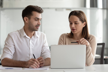 Confident businesswoman mentor teaching new employee, using laptop