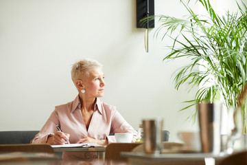 Mature businesswoman with short blond hair looking away while working at the table at office