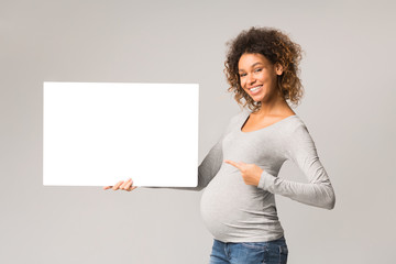 Happy afro pregnant woman pointing at blank advertising sheet
