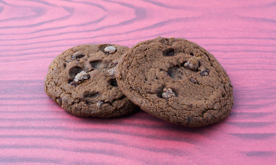 Two double chocolate chip cookies on a purple pattern background