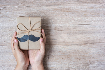 holding gift box with mustache on wooden background, preparation for fathers. World International men day and Father’s day concept