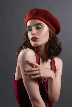 Beautiful girl wearing french style red beret and body, and black stockings elegantly poses on the gray background. Fashionable, advertising, art design.
