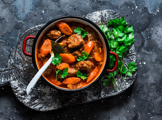 Cozy comfort winter autumn food - spicy braised crock pot beef in a pot on a rustic wooden board on a dark background, top view