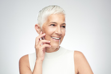 Beautiful smiling senior woman with short gray hair posing in front of gray background. Beauty photography.