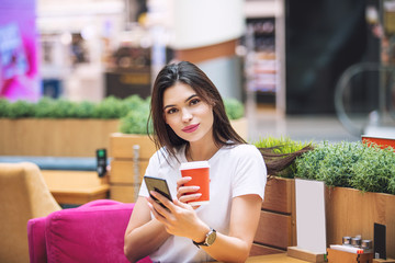 Young adult beautiful brunette girl happy sitting in cafe with coffee and mobile phone