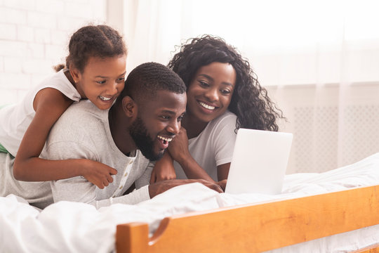 African family lying on bed browsing internet on laptop together