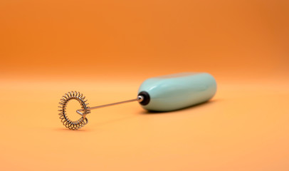 Hand held beverage mixer Focus on the blade with a blender on orange background