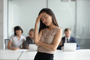 Unhappy Asian businesswoman suffering from headache, touching forehead