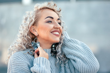 Plus size model with blond curly hair in knitted sweater and silver earrings outdoor
