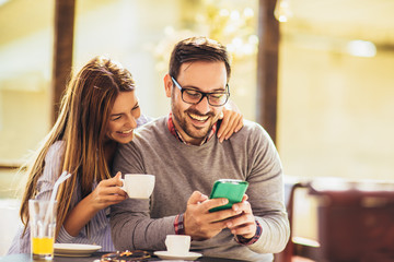 Young cheerful man and woman dating and spending time together in cafe, using phone.