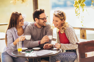 Cheerful group of friends having fun in cafe, using digital tablet.