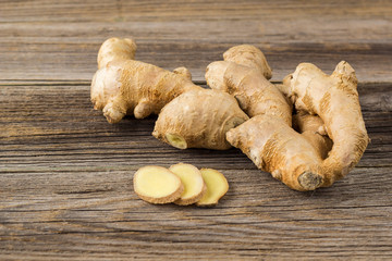 A root of ginger with sliced pieces on a wooden background