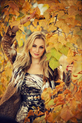 Naklejka na ściany i meble Outdoor fashion art photo of young beautiful blonde woman surrounded autumn leaves outdoor in park. Autumn season fashion concept