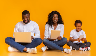 Happy black family using different gadgets, sitting on floor together