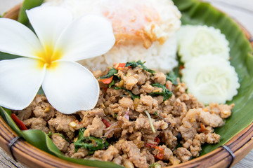 close up of the most popular Thai food with rice and fried pork with basil on banana leaf and wood plate.