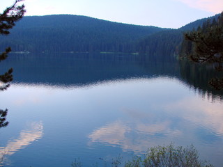 Panorama of blue sky covered with small clouds in the reflection on the water surface of a calm mountain lake.