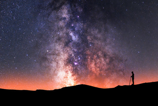 Man silhouette standing on the hill. Behind him beautiful milky way galaxy. Night photography.