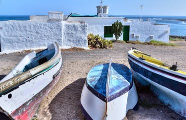 Fishing boats on the sandy beach and  white washed building with green wooden door and window at the background, Teguise, Lanzarote, Canary Islands, Spain