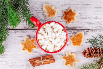 Obraz na płótnie Canvas Red cup with hot cocoa and marshmallows, cinnamon sticks, toasted shaped bread slices on wooden table in Christmas New Year season decorations with fir tree and cone. Cozy winter breakfast concept.