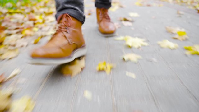A young man in leather shoes is walking along a sidewalk with fallen leaves. Fall season. Outdoor city walk concept. Slow motion