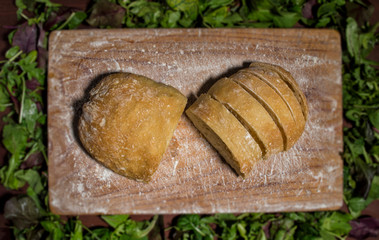 Italian ciabatta bread on kitchen wooden board. Around the board frame with herbs. Top view