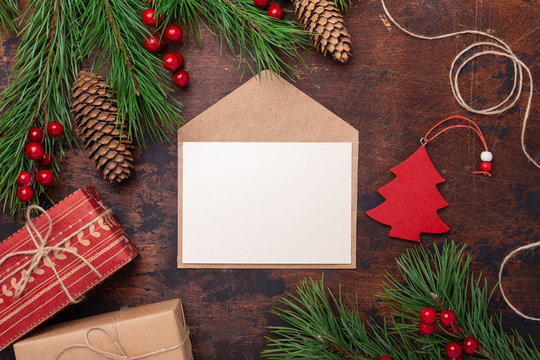 Christmas greeting card with fir tree branch, gifts, present box and envelope. Wooden background Top view, copy space.