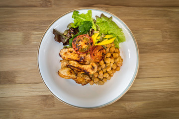 Grilled chicken with chickpeas and salad on a wooden background