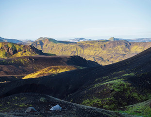 Three tents alone in Botnar campsite at Iceland on Laugavegur hiking trail, green valley in volcanic landscape among lava fields with view on Myrdalsjokull glacier. Early morning sunrise light