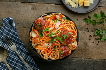 Delicious spaghetti pasta with meatballs and tomato sauce in a bowl. Traditional American Italian food on a rustic wooden table. Top view shot.