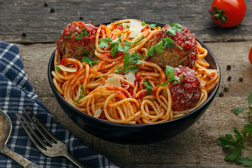 Pasta with meatballs, parmesan and tomato sauce in a clay bowl. Homemade Italian spaghetti on a rustic wooden table.