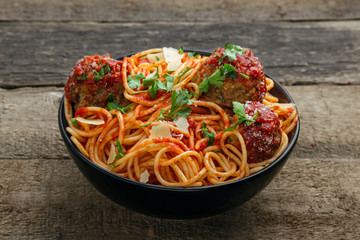 Delicious spaghetti pasta with meatballs and tomato sauce in a bowl. Traditional American Italian food on a rustic wooden table.