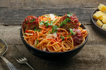 Spaghetti with meatballs, parmesan and tomato sauce in a bowl on a rustic wooden table. Tasty Italian pasta food.