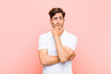 young handsome man thinking, feeling doubtful and confused, with different options, wondering which...