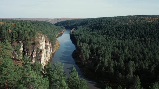 High steep cliffs of curved Ural river Ay; natural landscape with mixed forest on riversides; autumn colored orange yellow birches; aerial view, drone flying over tree crones; bright fall season day