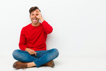 young handsome man smiling happily with funny face, joking and looking through peephole, spying on...
