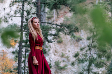 Naklejka premium Girl in a burgundy dress in a pine forest.