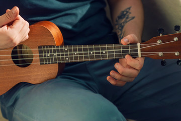 A man in blue clothes and with a tattoo on his arm plays a cheerful tune on a ukulele on a Sunny...