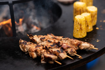 cooking, frying meat and corn in a huge flat pan with an open fire in the middle