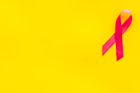 Pink ribbon as symbol of breast cancer awareness on yellow background top view copy space