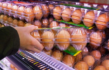 Buying eggs in a supermarket. Buyer holds in his hand a package of raw chicken eggs.