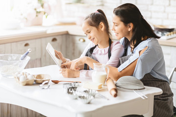Mother and daughter holding digital tablet checking recipe of dough