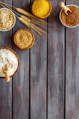 Set of cereals - rice, oats, buckwheat - in bowls with ears on dark wooden background top view frame copy space