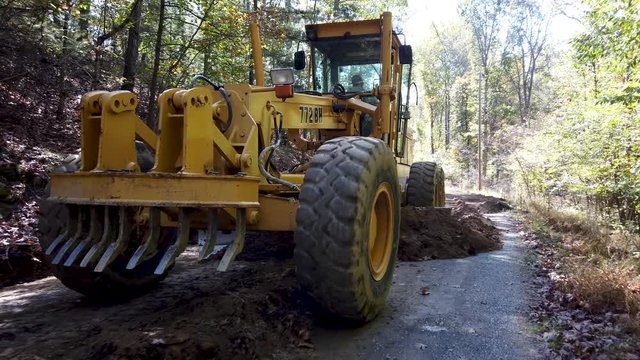 Closeup of front wheels of road grader as it scrapes fresh dirt to make a road.