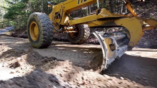 Closeup side shot of road grader scraper, scraping dirt for making a road.