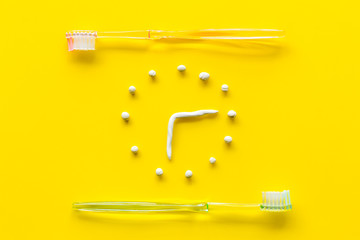 Time to brushing teeth. Watches near teethbrushing on yellow background top view