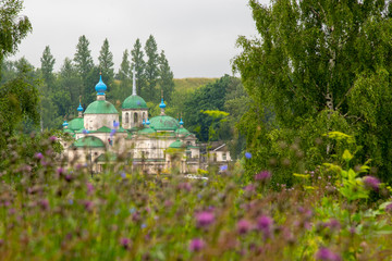 In the foreground, a blur of wild wildflowers, through which you can see a Church and trees.